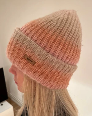 Stickad mössa i rosa och beige från Barts - Säljer en ribbstickad mössa från Barts i mjuka nyanser av rosa och beige. Den är köpt i valdisere för ca 850kr🩷