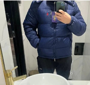 Mörkblå pufferjacka från Polo - Säljer en mörkblå pufferjacka från Polo med röd logga på bröstet. Jackan har huva, dragkedja framtill och två sidofickor med dragkedja. Perfekt för kalla dagar och riktigt snygg passform.