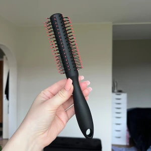 Rund hårborste - Detta är en svart rund hårborste med röda kulor på piggarna, perfekt för styling och föning. Borsten är i fint skick utan synligt slitage eller defekter. Ergonomiskt handtag med hål för upphängning. Passar både för att skapa volym och för att reda ut håret. Köper du innan kl 16:00 kan jag posta samma dag!