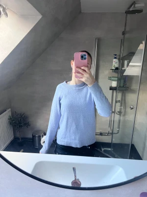 Ljusblå stickad tröja med rund hals - Säljer en ljusblå stickad tröja med rund hals och ribbade muddar. Tröjan har en enkel och clean design med lång ärm och normal passform. Perfekt för dig som gillar en chill och stilren look.