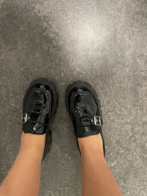 Chunky svarta loafers med spänne - Säljer ett par chunky svarta loafers med grov platt sula och blank finish. 