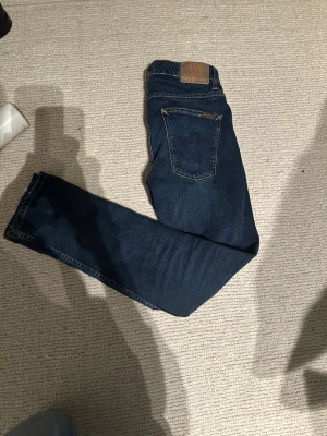 Nudie Jeans Grim Tim New Ink W31/L32 - Säljer ett par Nudie Jeans Grim Tim i modellen New Ink. Mörkblå denim med klassiska kontrastsömmar och bakficka med Nudie-logga. Nypris är 1600 på Nudie hemsida!🙌Snygg rak/slim passform som passar till utmärkt vardagslooken. Populär modell New Ink, snygg och fin mörkblå tvätt. Jeansen är i nyskick med inga skavanker eller liknade. Storlek W31/L32. Pris är diskuterbart mot en snabb och enkel affär🙌☀️