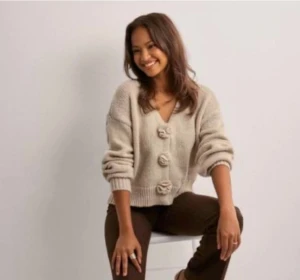 Beige stickad kofta med blommiga knappar - Superfin beige stickad kofta med v-ringning och stora, blommiga knappar framtill. Koftan har en loose passform och långa ärmar med ribbade muddar. Perfekt för lager-på-lager och chill stil. Köpt från Nelly för 399kr. 