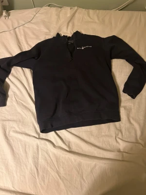 Mörkblå Sail Racing half zip tröja - Mörkblå långärmad tröja från Sail Racing med half zip och liten logga på bröstet samt i nacken. Tröjan har en hög krage och är tillverkad i mjukt material som känns skönt mot huden. Perfekt för dig som gillar stilren och sportig look.