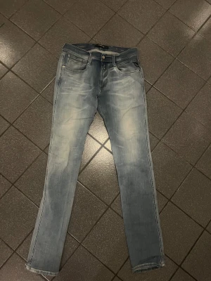 Replay Hyperflex Anbass ljusblå jeans - Säljer ett par Replay Hyperflex Anbass jeans i ljusblå tvätt. De har klassisk femficksdesign, smal passform och stretchigt material för extra komfort. Perfekta för dig som gillar en modern och stilren look. Midjan är normal och benen är raka med lätt slitning framtill. 