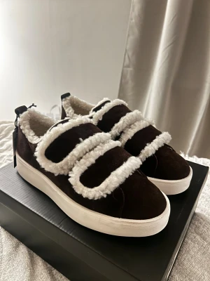 Mörkbruna sneakers från Duffy, strl 38 - Snygga mörkbruna mocka sneakers från Duffy med vit fluffig fuskpäls längs kanterna. Skorna är nya och kvitto finns🫶nypris 900kr