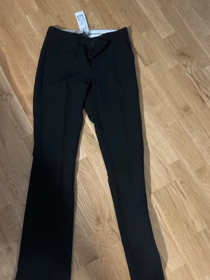 Svarta kostymbyxor från Neo Noir - Snygga svarta kostymbyxor från Neo Noir med klassisk rak passform och pressveck. Byxorna är ej använda