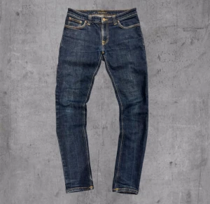 Mörkblå jeans från Nudie Jeans Co W31 L32 - Snygga mörkblå jeans från Nudie Jeans Co med klassisk femficksdesign och kontrastsömmar i gult. Modellen har rak passform och normal midja. Materialet är slitstarkt jeans och färgen är djup blå med lätt tvättad look. Perfekt för dig som gillar stilrena och tidlösa jeans.