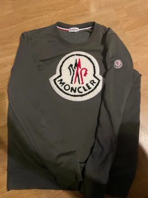 Mörkgrön sweatshirt från Moncler - Snygg mörkgrön sweatshirt från Moncler med stort broderat logomärke i vitt, svart och rött på bröstet samt mindre logga på ärmen. Rund hals och långärmad modell, tillverkad i mjuk bomull. Perfekt för dig som gillar exklusiva streetwear-vibes. ÄKTA!!!!!