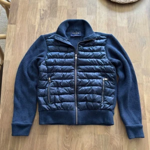 Blå quiltad pufferjacka från Vonroe - Snygg mörkblå pufferjacka från Vonroe med stickade ärmar och rygg. Framsidan är quiltad med två dragkedjeförsedda fickor och hel dragkedja. Jackan har en ribbad krage och muddar, perfekt för dig som gillar en sportig och modern look.