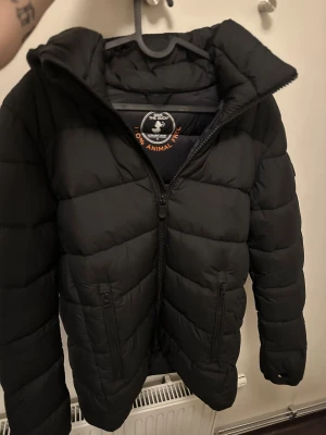 Save the duck jacka - Säljer en svart pufferjacka från Save The Duck i storlek S. Jackan är quiltad, har huva och dragkedja framtill samt två praktiska fickor med dragkedja. Tillverkad i syntetmaterial och helt animal free. Perfekt för kalla dagar och riktigt snygg passform.