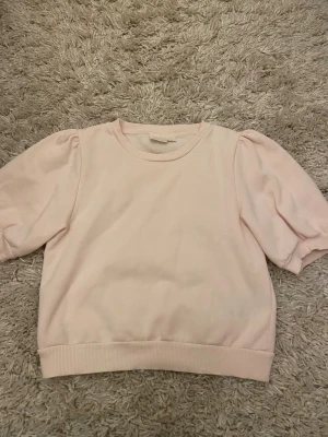 Ljusrosa puffärm tröja Gina Tricot - Supersöt ljusrosa tröja från Gina Tricot med puffiga korta ärmar och rund hals. Tröjan har ribbade muddar vid hals, ärmslut och nederkant. Perfekt för dig som gillar en enkel men ändå trendig look.