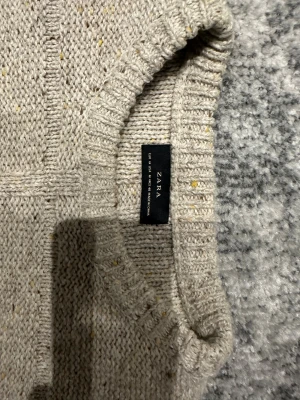 Beige stickad tröja från Zara - Säljer en beige stickad tröja från Zara med diskreta gula och bruna detaljer i garnet. Tröjan har rund hals, ribbade muddar och långärmad passform. Perfekt för dig som gillar enkel och clean stil med lite textur.