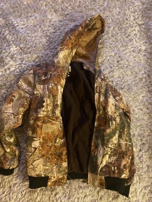 Carhartt camo vintage jacka med huva - Säljer en fet camo pufferjacka från Carhartt med huva och quiltat foder. Jackan har dragkedja, muddar vid ärmslut och midja samt två stora fickor fram. Perfekt för dig som vill sticka ut med en skogsinspirerad look.