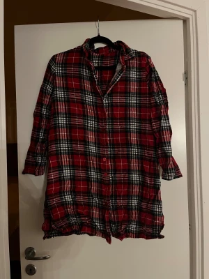 Nattskjorta från Ellos - Rutig nattskjorta från Ellos i rött, svart och vitt. Långärmad modell med knappar framtill och krage. Fint skick!
