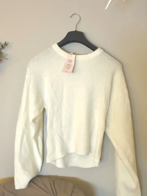 Figursydd Vit stickad tröja  - Mysig vit stickad tröja från Nelly med rund hals och långärmad design. Tröjan har en fluffig och mjuk känsla, perfekt för kyliga dagar. Enkel och stilren look som är lätt att matcha med dina favoritjeans eller kjol.