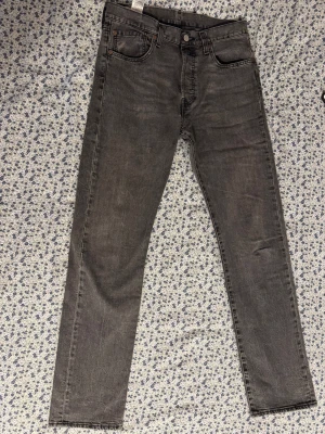 Levi's 501 svarta jeans W31 L34: Bra skick! - Säljer ett par klassiska Levi's 501 jeans i svart tvätt. Jeansen har rak passform, fem fickor och knappgylf. De är tillverkade i slitstarkt bomullsjeans och har den ikoniska läderpatchen bak i midjan. Perfekta för en avslappnad och tidlös look.