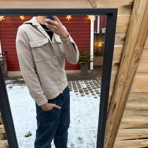 Beige overshirt med fickor - Säljer en beige overshirt med klassisk krage och stora bröstfickor med lock. Skjortan har knäppning framtill och är långärmad. Perfekt att slänga över en t-shirt för en chill look.