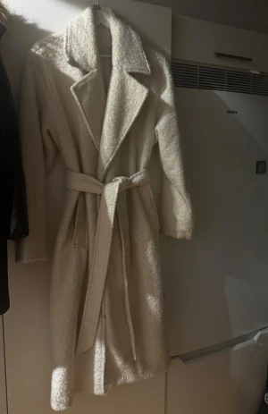 Beige teddykappa med bälte - Säljer en jättefin lång, beige teddyjacka med bred krage och knytskärp i midjan. Jackan har en mysig, fluffig textur ”teddymaterial”. Använd ett fåtal gånger. Säljer för 250kr