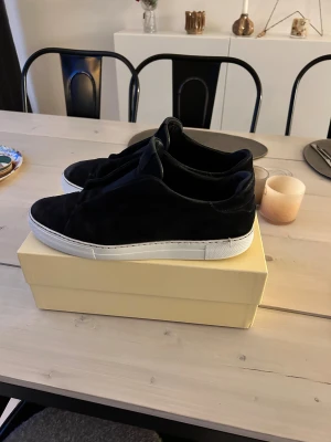 Axel Arigato Clean 360 - Snygga marinblåa sneakers i mocka med vit platt sula. Skorna har en minimalistisk design utan synlig snörning och en rund tå. Perfekta för dig som gillar stilrena och moderna skor med en mjuk känsla. 💸💸Dessa säljs inte längre / discontinued 💸💸 ⚠️Obs sulkräm har använts. ⚠️