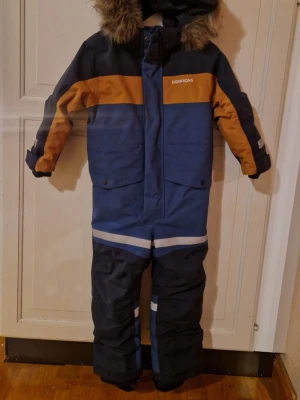  Didriksons Bjärven Overall storlek 100 - Säljer en blå overall från Didriksons i storlek 100 med snygga orange detaljer och reflexband. Endast använd 5ggr pga att fel storlek. 
