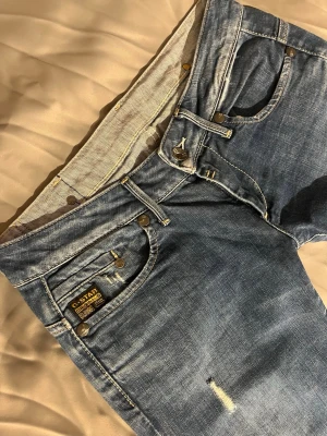 G-Star RAW – very low rise - Storlek 31/34 • Låg midja • Snygg tvätt • Mycket bra skick!!  Riktigt fina G-Star-jeans med låg midja och raka ben. Klassisk blå denim med stilrena slitdetaljer och ikoniska G-Star-sömmar. Sitter supersnyggt!😍  Säljer dem bara för att de tyvärr är för små för mig – annars hade jag behållt dem.!!  Mått:  Midja: 40cm Innerben: 82-83cm Bredd nertill: 18,5cm Lårbredd: 25cm Midjehöjd: 18,5 från söm mellan benen och upp (väldigt lowrise)