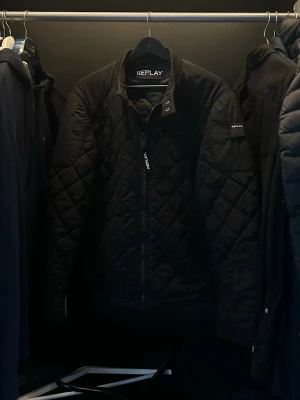 Svart jacka från Replay - Säljer en svart jacka från Replay med dragkedja framtill och Replay-logga på ärmen. Jackan har ribbade muddar och ett rutigt mönster. Perfekt för dig som vill ha en stilren och bekväm jacka.