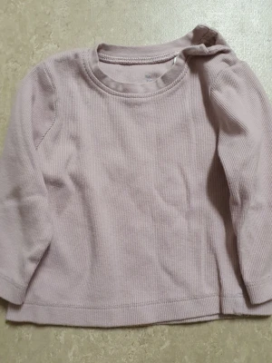 Tröja - Supersöt ljuslila långärmad tröja från I Love Eco i mjuk ekologisk bomull. Tröjan har ribbad struktur och praktiska tryckknappar på axeln för enkel påklädning. Perfekt basplagg till garderoben!