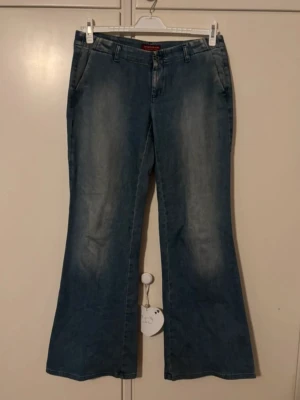 Blå bootcut jeans från Americanos - Snygga blå bootcut jeans från Americanos med klassisk femficksdesign och bälteshällor. Jeansen är tillverkade i 99% bomull och 1% elastan för en skön passform. De har en lätt tvättad look och är perfekta för dig som gillar retrostil.
