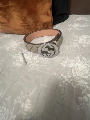 Gg Supreme bälte beige - Säljer ett klassiskt  GG Supreme bälte i beige med det ikoniska GG-mönstret och stor silverfärgad GG-spänne. Bältet är gjort i skinn och har detaljer i syntet. Perfekt accessoar för att lyfta vilken outfit som helst English.