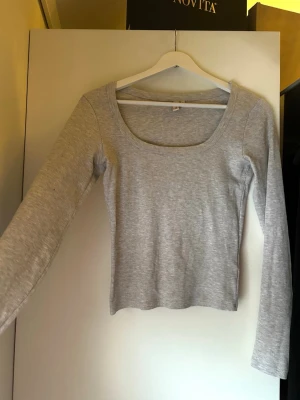 GRÅ TOPP: NELLY 🩶 - Långärmad grå topp i mjukt, följsamt material med cropped längd. Minimalistisk och lättstylad – perfekt för både vardagslooks och avslappnade hemmadagar.