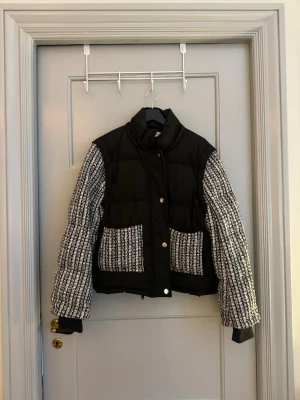 CLOEYS Svart tweed pufferjacka med huva/ väst - Säljer en svart pufferjacka med tweed-detaljer på ärmar och fickor. Jackan har hög krage, avtagbar huva, avtagbara ärmar och stora framfickor. Stängs med knappar framtill och har en cool, boxig passform. Snygg även som väst när man tar av ärmarna. 
