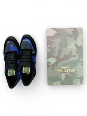 Valentino Rockrunner blå camo sneakers - Säljer ett par Valentino Rockrunner sneakers i blått och svart med camouflagemönster. Skorna har svarta snören, detaljer i mocka och skinn samt en cool platt sula. Perfekta för dig som vill sticka ut med en unik och trendig look.