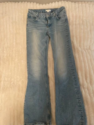 Ljusblå bootcut jeans med rå kant - Säljer ett par ljusblå jeans. Perfect Jeans med bootcut-modell. Jeansen har klassisk femficksdesign och är tillverkade i mjukt denimtyg. Perfekta för dig som gillar en avslappnad och trendig look. OBS! Är lite slitna nere till men ser bara ut som en fin detalj.