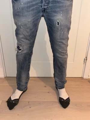 Ljusblåa jeans med slitningar - Säljer ett par blå jeans från Jack & Jones med slitningar. Slim fit