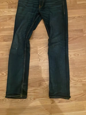 Jack & Jones mörkblå jeans Clark 29/32 - Säljer ett par mörkblå jeans från Jack & Jones, modell Clark Regular. Jeansen har klassisk femficksdesign, kontrastsömmar och raka ben. Materialet är slitstarkt denim i bomull. Perfekt passform för dig som gillar en normal och tidlös stil.