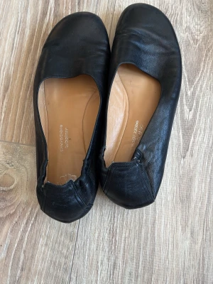 Svarta ballerinaskor i skinn - Klassiska svarta ballerinaskor i mjukt skinn med rund tå och elastisk kant. Insidan är beige och har texten 'lavorazione tubolare'. Skorna har platt sula och enkel, stilren design som passar till det mesta.