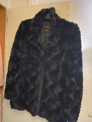 Svart pälsjacka med krage - Säljer en svart pälsjacka med snygg krage och knäppning framtill. Jackan har en fluffig och lyxig känsla, perfekt för att sticka ut i mängden. Långärmad modell som håller dig varm under kyliga dagar. Passar dig som gillar statement-plagg.