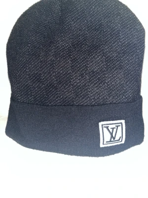 Mörkblå Louis Vuitton mössa - Jag säljer denna mörkblåa louis Vuitton mössan för priset av 250kr. Den är i otroligt skick, endast använd någon enstaka gång, samt håller dig varm över vintern och den kyliga våren. Skriv vid minsta fundering.