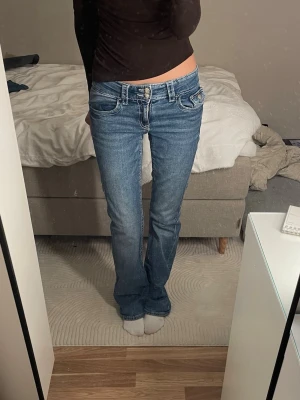 Blå bootcut jeans med låg midja - Lågmidjade Bootcut jeans med dubbelknapp framtill från Gina.💕                             Innerbenslängd: 83cm                                 Midjemåttet: 35cm                                           Grenhöjd: 19cm