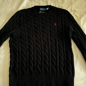 Svart kabelstickad tröja Polo Ralph Lauren - Säljer en svart Polo Ralph Lauren kabelstickad tröja med dragkedja i storlek S. Aldrig använd och i nyskick, prislapp kvar. Hör av dig vid intresse!