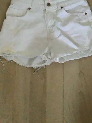 Vita fransiga shorts från Zara - Säljer ett par vita shorts från Zara med råa, fransiga kanter och klassisk femficksdesign. Shortsen har hög midja, bälteshällor och stängs med knapp och dragkedja. Perfekta för sommardagar och har en clean look.