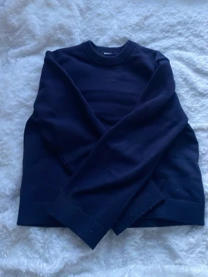 Mörkblå stickad tröja - En stilren mörkblå stickad tröja. Klassisk rund halsringning och ribbade muddar vid ärmslut och nederkant. Perfekt till lager på lager under höst och vinter. Enkel att matcha med jeans eller kjol. Tröjan är nopprig på vissa ställen