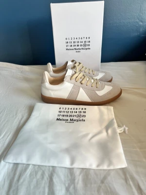 Maison Margiela gats - Maison Margiela gats i vit och beige med klassisk gummisula. Ovandel i skinn och mocka, med beige snörning och rund tå. Snygg retrostil och diskreta detaljer, levereras med originalkartong och dustbag. Perfekt för dig som gillar minimalistisk design. 0bs lnte 0rglnal‼️