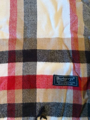 Rutig halsduk från Burberrys i ull - Snygg klassisk halsduk från Burberrys med det ikoniska rutmönstret i beige, svart, rött och vitt. Tillverkad i 100% lammull och har fransar i kanterna. Perfekt för att ge din outfit en lyxig touch och hålla dig varm under kyliga dagar.