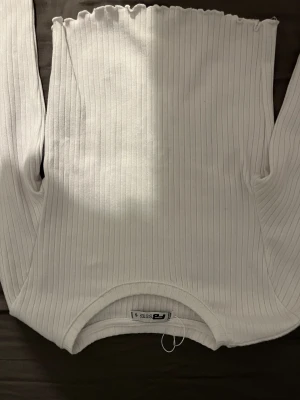 Vit ribbad långärmad tröja från FB Sister, newyorker  - Vit långärmad tröja från FB Sister i storlek S. Tröjan är ribbad med smala vertikala ränder och har en söt vågig kant vid halsringningen och ärmsluten. Materialet är mjukt och stretchigt, perfekt för att skapa en clean och fräsch look.