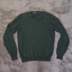 Grön merinoullströja från Alan Paine stl XL - Mörkgrön stickad tröja från Alan Paine i 100% merinoull. Klassisk v-ringad modell med lång ärm och ribbade muddar. Perfekt för lager-på-lager och snygg till både jeans och chinos.