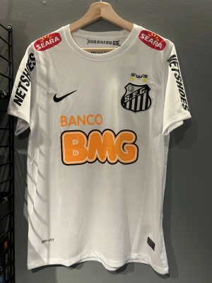 Santos Neymar Jr matchtröja Nike S - Säljer en officiell Santos FC fotbollströja med Neymar Jr och nummer 11 på ryggen. Tröjan är vit med svarta och orange tryck, klubbmärke på bröstet och flera sponsorer. Tillverkad i lätt Dri-Fit material, kortärmad och med rund hals. Perfekt för dig som älskar brasiliansk fotboll. Helt ny tröja med tagg en replika