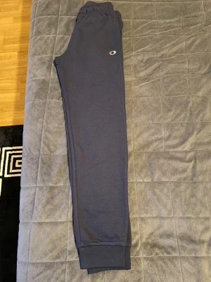 Mörkblå mjukisbyxor från Champion barnkläder 155 cm. 12 year  - Mörkblå mjukisbyxor från Champion med broderad logga på vänster lår. Byxorna har resår och snörning i midjan samt muddar vid bensluten. Tillverkade i mjukt bomullsmaterial för maximal komfort. Perfekta för chill eller träning.