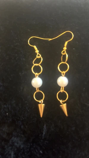 Guldiga örhängen med pärlor och spikes - Unika örhängen med guldiga ringar, vita pärlor och coola konformade spikes längst ner. Perfekt för dig som vill sticka ut med en edgy men ändå elegant stil. Hängande modell som ger extra attityd till din look.